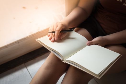 Young woman reading blank book while sitting beside window in morning time on weekend. Morning lifestyle on weekend concept.