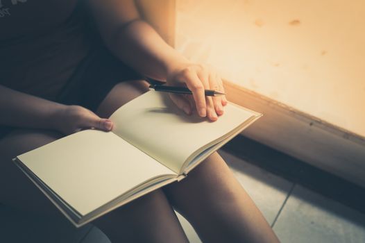 Young woman reading blank book while sitting beside window in morning time on weekend. Morning lifestyle on weekend concept with vintage filter effect