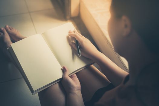 Young woman reading blank book while sitting beside window in morning time on weekend. Morning lifestyle on weekend concept with vintage filter effect