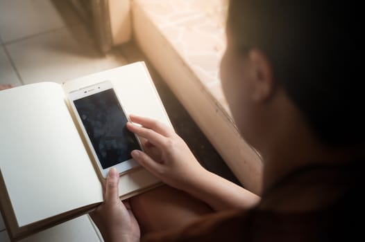 Young woman using smartphone while reading book in morning time on weekend. Morning lifestyle with technology on weekend concept.