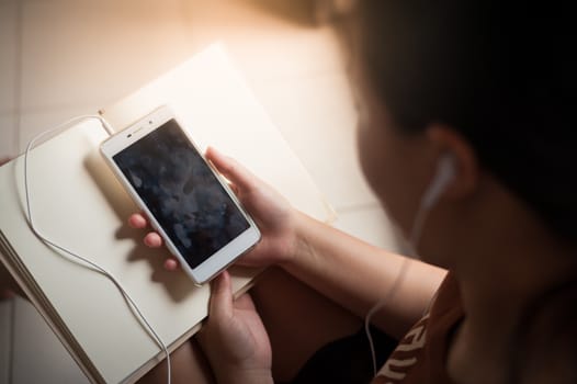 Young woman listening music with smartphone while reading book in morning time on weekend. Morning lifestyle with technology on weekend concept.