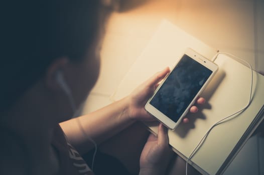 Young woman listening music with smartphone while reading book in morning time on weekend. Morning lifestyle with technology on weekend concept with vintage filter effect