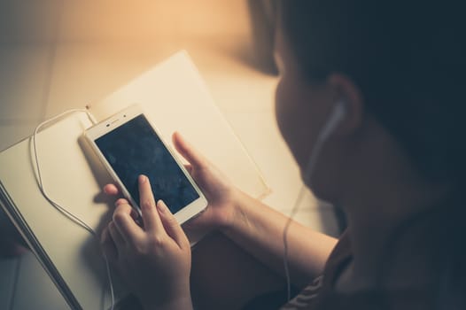 Young woman listening music with smartphone and touching on screen while reading book in morning time on weekend. Morning lifestyle with technology on weekend concept with vintage filter effect