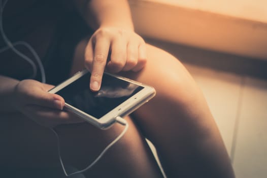 Young woman touching on smartphone screen by left hand while listening music in morning time on weekend. Morning lifestyle with technology on weekend concept with vintage filter effect