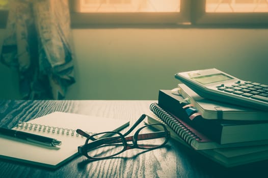 Glasses put down on table beside notebooks and pen in morning time on work day. Freelance business working concept with vintage filter effect