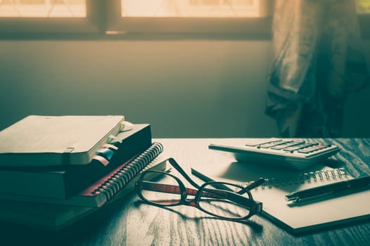 Glasses put down on table beside notebooks and pen in morning time on work day. Freelance business working concept with vintage filter effect