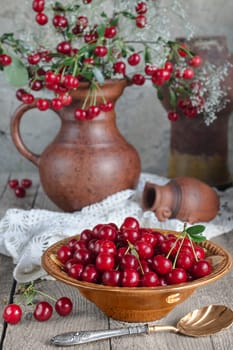 Cherries in the bowl and the bouquet on the old boards. Ceramic kitchenware, vintage spoon and gray background.