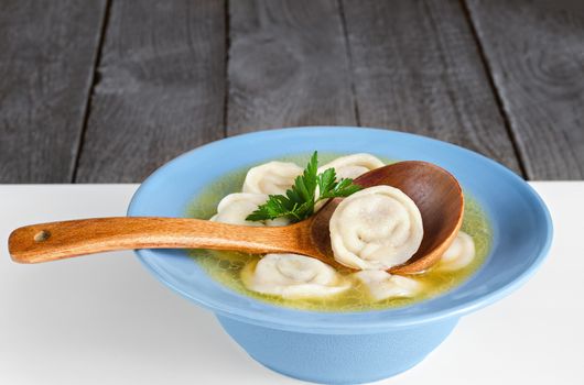 Dumplings with broth in a bowl and a wooden spoon.