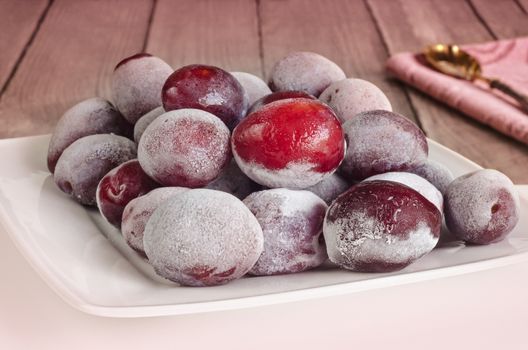 Frozen plums on plate, on wooden background toned in pink