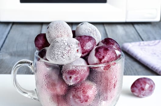 Frozen plums in a glass Cup on the background of the microwave.