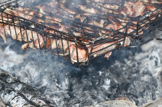 Pork meat fried on grill, on the coals of a campfire.