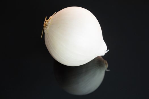 Three whole fresh raw white onions on a reflective black background with copy space