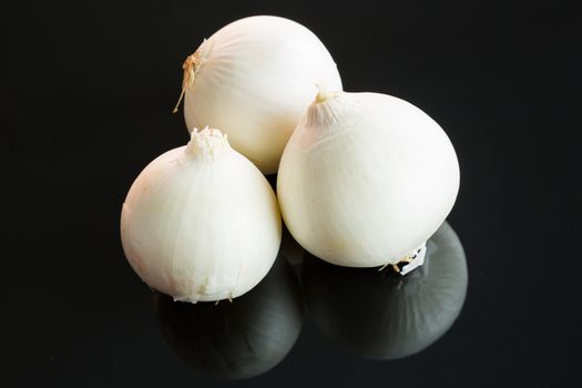 Three whole fresh raw white onions on a reflective black background with copy space