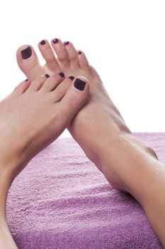 Bare feet with pedicure propped by towel on soft purple treatment table against white background