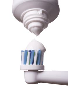 Close up of electric toothbrush with blue bristles and tube with paste bubbled at its opening on white background