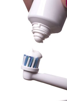 Close up of electric toothbrush with blue bristles and tube with paste bubbled at its opening on white background