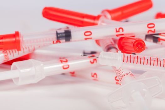 Still Life Close Up of Pile of Empty Syringe Needles with Red Safety Caps in Studio with White Background