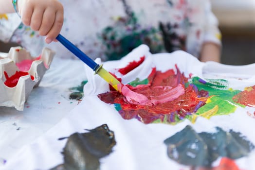 Child hands using paintbrush painting on t-shirt.