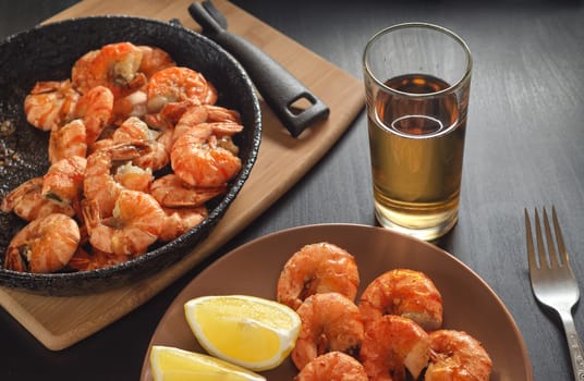 Dish and pan with fried shrimp, lemon and beer in glass on black table.