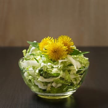 White cabbage salad in a glass vase decorated with dandelions. . Low key.