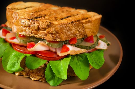 Big sandwich with ham, cheese, tomatoes, pickles and herbs. On a black background.