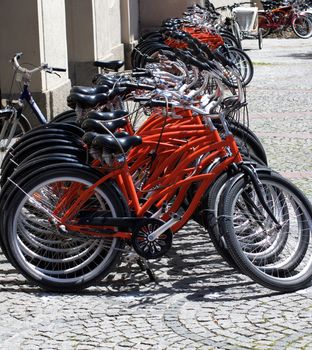 Arrangement of Parked Rental Bicycles on Paving Stone Sidewalk in Summer Day in Europe Outdoors