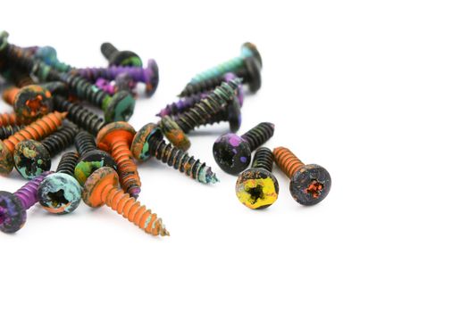 Crosshead screws, covered in messy colourful paint, in shallow focus on a white background
