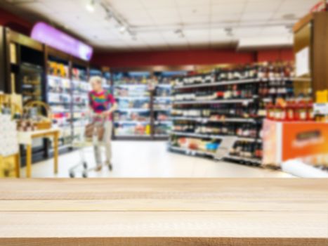 Wooden board empty table in front of blurred background. Perspective light wood over blur in supermarket with unrecognizable customer. Mock up for display or montage of product.