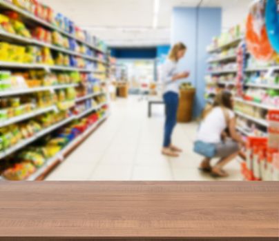 Wooden board empty table in front of blurred background. Perspective brown wood over blur in supermarket with unrecognizable customer. Mock up for display or montage of product.