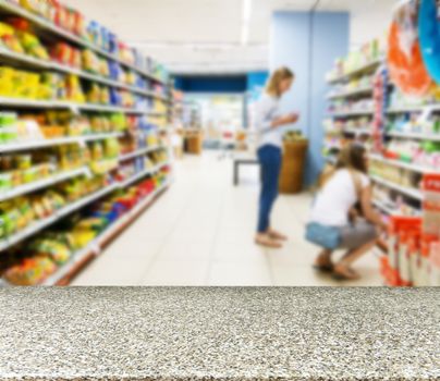 Marble board empty table in front of blurred background. Perspective marble table over blur in supermarket with unrecognizable customers. Mock up for display or montage of product.