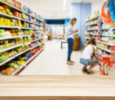 Wooden board empty table in front of blurred background. Perspective light wood over blur in supermarket with unrecognizable customer. Mock up for display or montage of product.