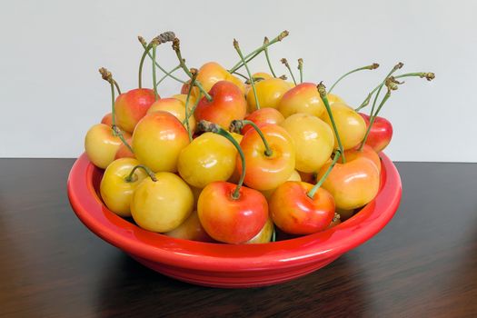 Pile of Rainier Cherries in a red bowl and on a wooden table macro