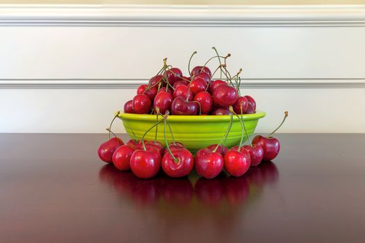 Pile of Bing Cherries in green bowl and on wood table with reflection