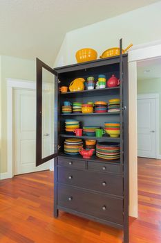 Cupboard with colorful stoneware dinnerware in home with cherry hardwood floor
