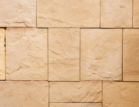 a wall from an artificial beige stone facade with rough fractured surfaces