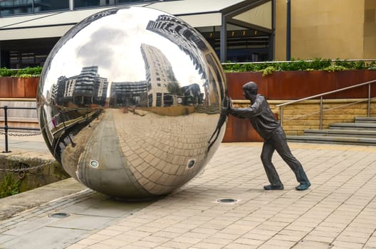 Monument as a Man pushing a huge  silver ball in Leeds Dock