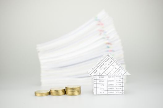 Close up step of gold coins and house have blur pile overload paperwork of report and receipt with colorful paperclip place on white background.