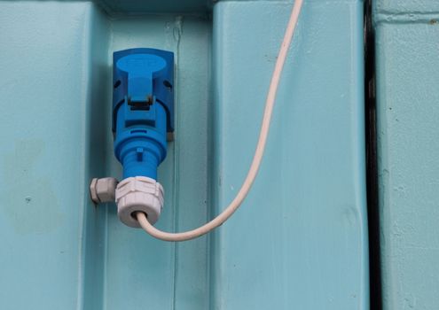 Outdoor Blue High Voltage Electrical Mount Plug with White Wire on Background of Steel Container