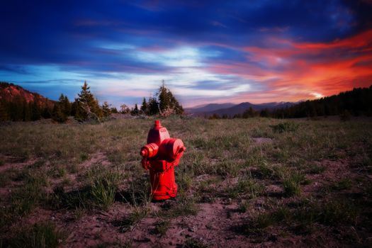 A red fire hydrant in the middle of a field with a colorful sunset in the background.