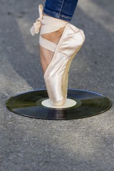 Foot girls in Ballet shoes  stands on a vinyl disc, which lies on the road.