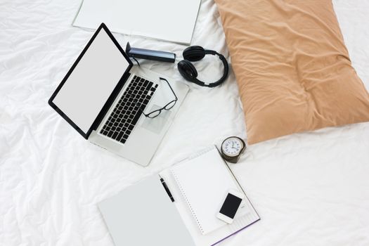 Blank screen notebook and workbook with pen, eyeglasses and wireless headphone on bed, work on bed concept