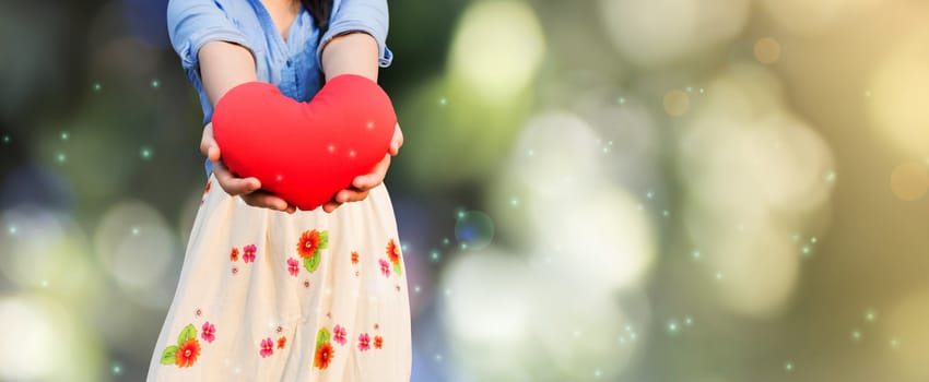 Girl presenting or giving big red heart on bokeh natural green background