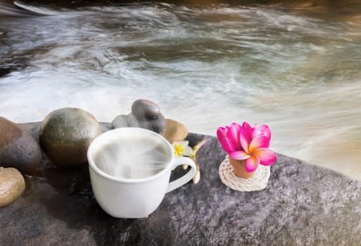 Dreamy white cup of hot black coffee on waterfall rock with flower and water nature view background in happy relax feeling morning light and copy space