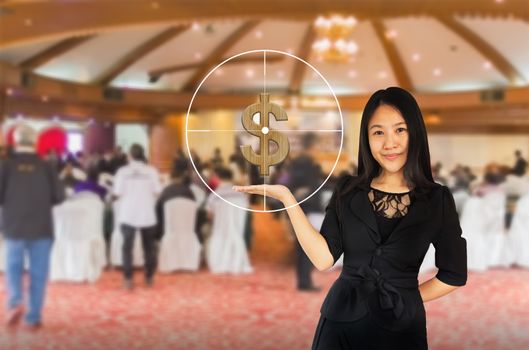 Smiling young Asian business women in black suit with dollar and target symbol on presenting hand on blurred background of meeting people