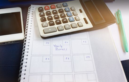  Organiser book with text yearly bonus and background of calculator and cellphone in dim light room