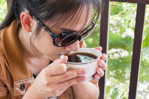 Asian women drinking hot coffee or tea in fresh happy morning light and tree bokeh background with copy space