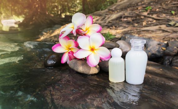 Mini set of bubble bath shower gel liquid with flowers and pebble on waterfall rock  with natural water relaxing feeling background and copy sapce