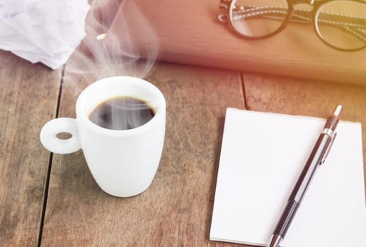 White cup of black coffee with blank note book and pencil on wood table