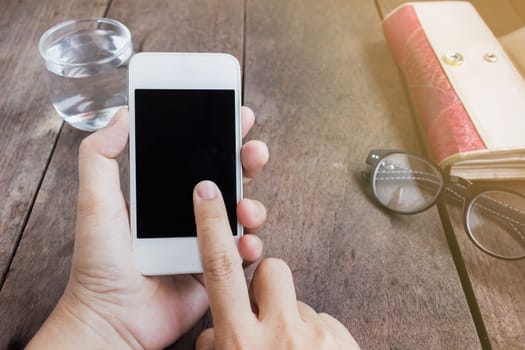 Lady hand serfing internet on mobile phone with background of things on wood table and copy space