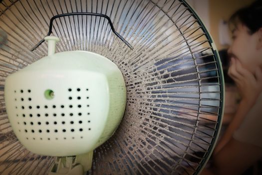 Dusty or unclean portable fan with blurred girl working at table